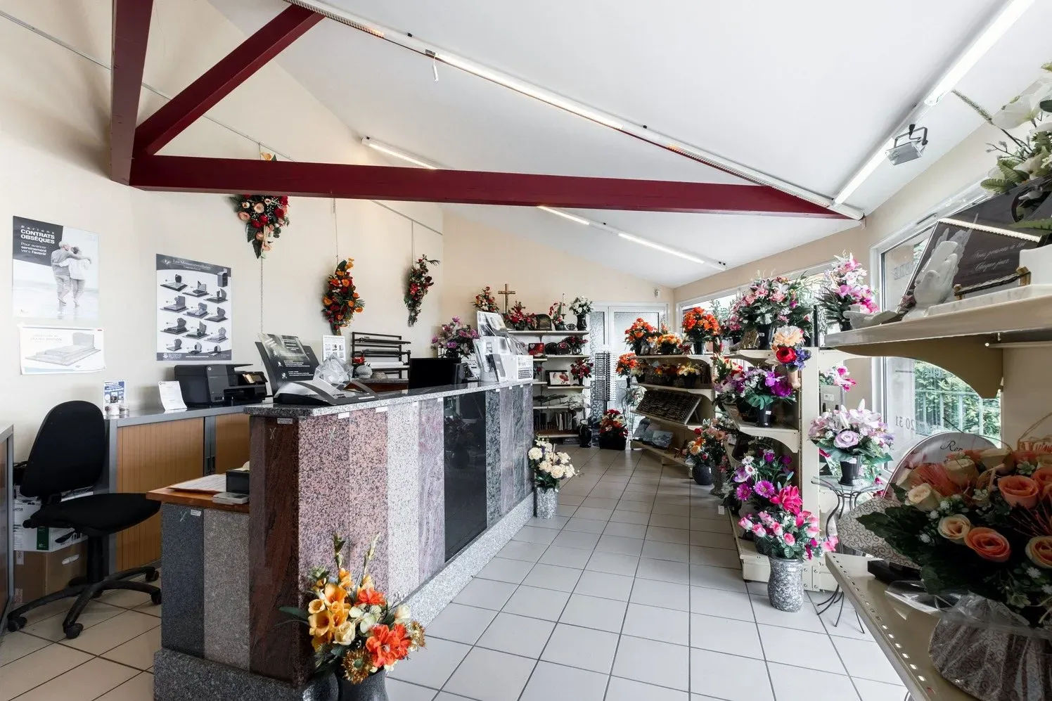 Intérieur de l'agence funéraire exposant des bouquets, articles funéraires et comptoir en granit.
