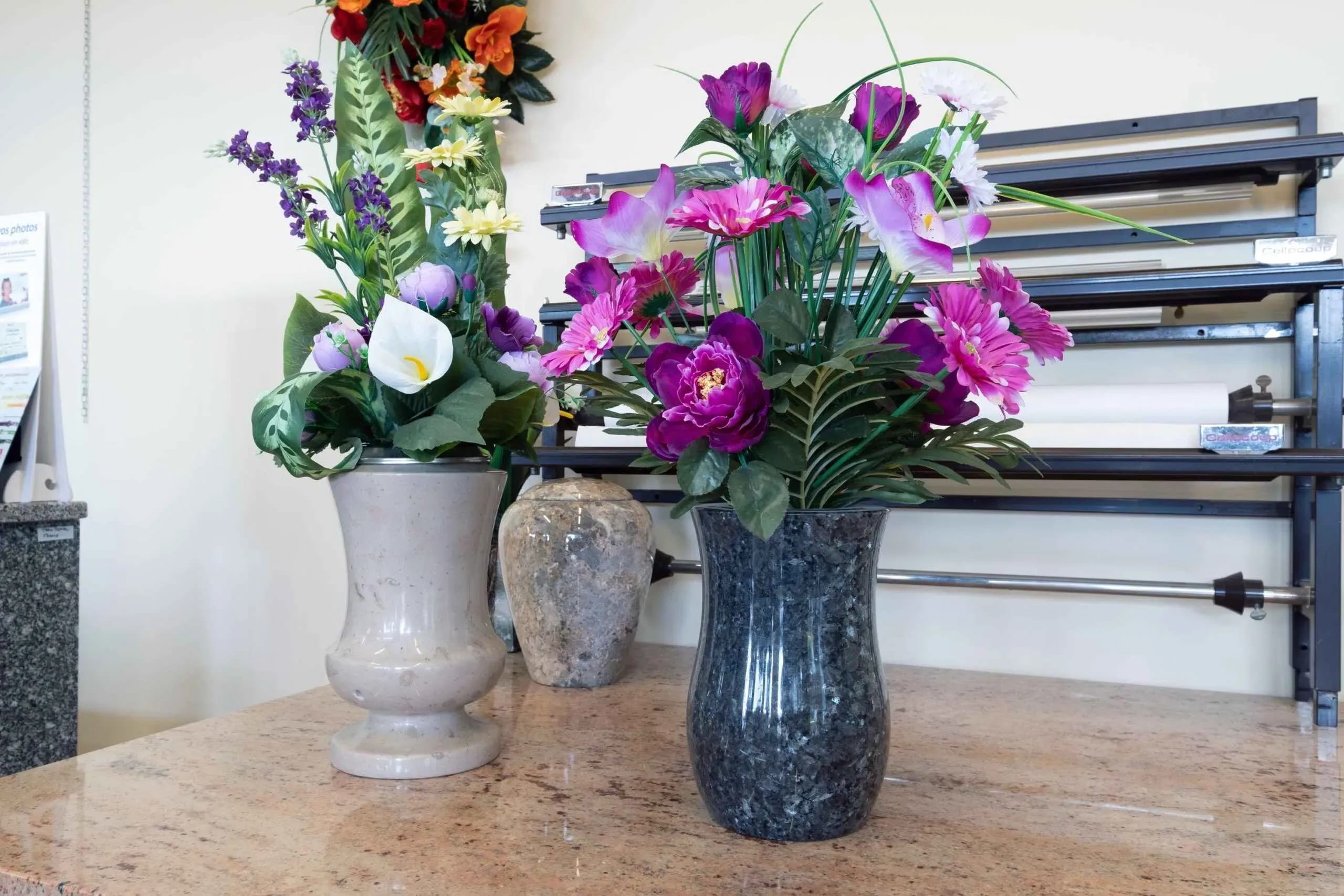 Vases funéraires en granit garnis de compositions florales colorées.