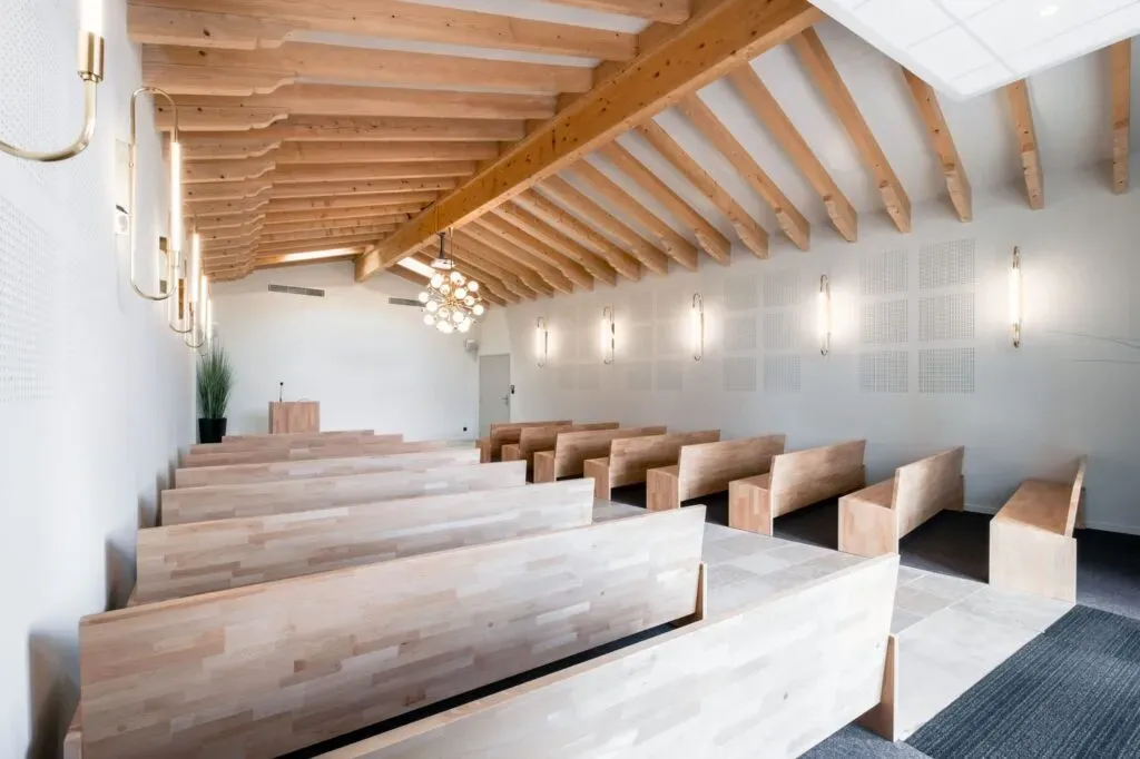 Grande salle de cérémonie funéraire lumineuse avec bancs et charpente en bois clair.
