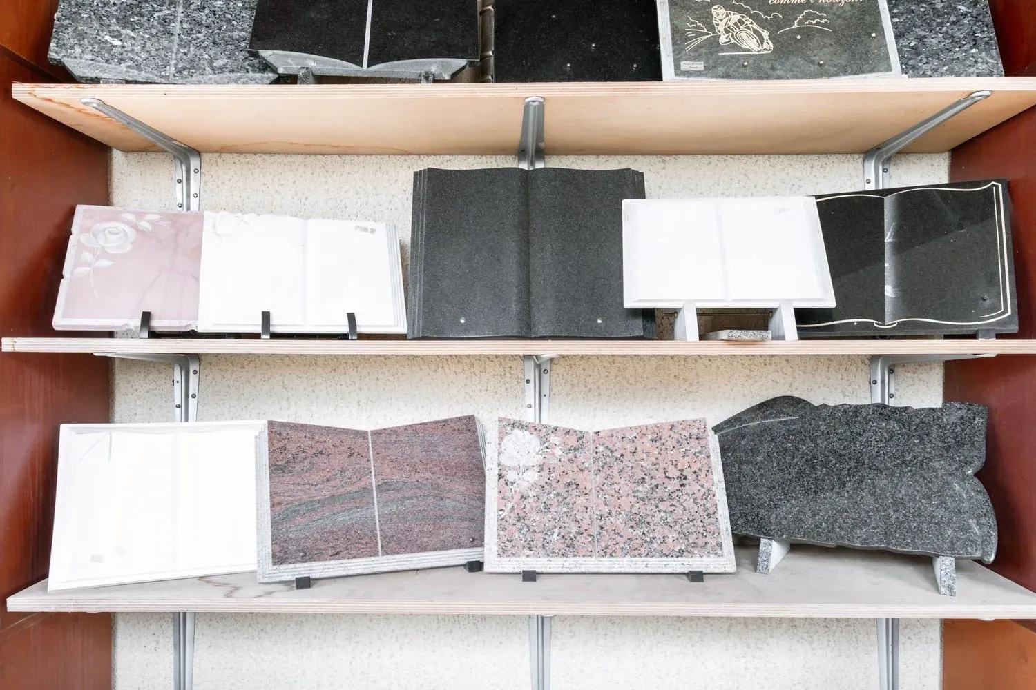 Étagères présentant un éventail de plaques funéraires en forme de livre en granit et en marbre.